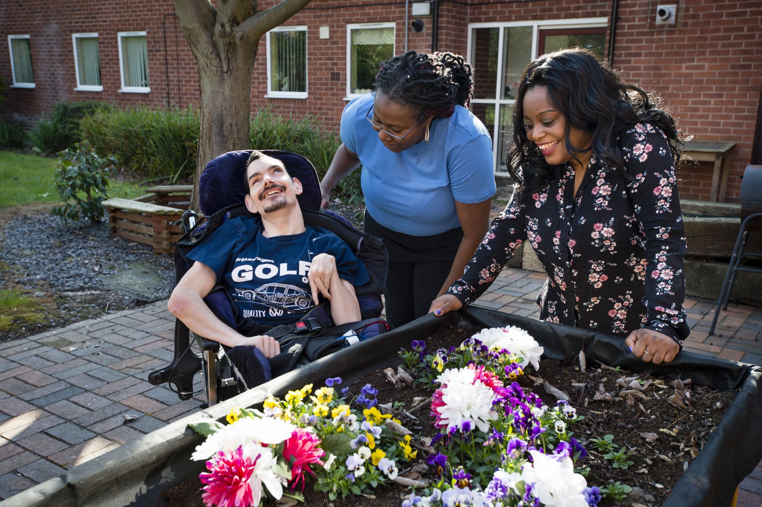 Person supported in wheelchair with two colleagues in garden.