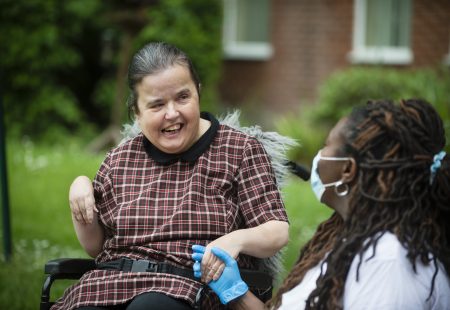 Person supported in wheelchair talking with colleague