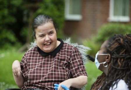 Person supported in wheelchair smiling at colleague