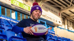 Oliver Thomason holding a Rugby League World Cup ball sat in the Halliwell jones stadium