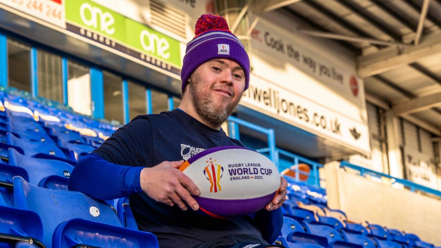 Oliver Thomason holding a Rugby League World Cup ball sat in the Halliwell jones stadium.