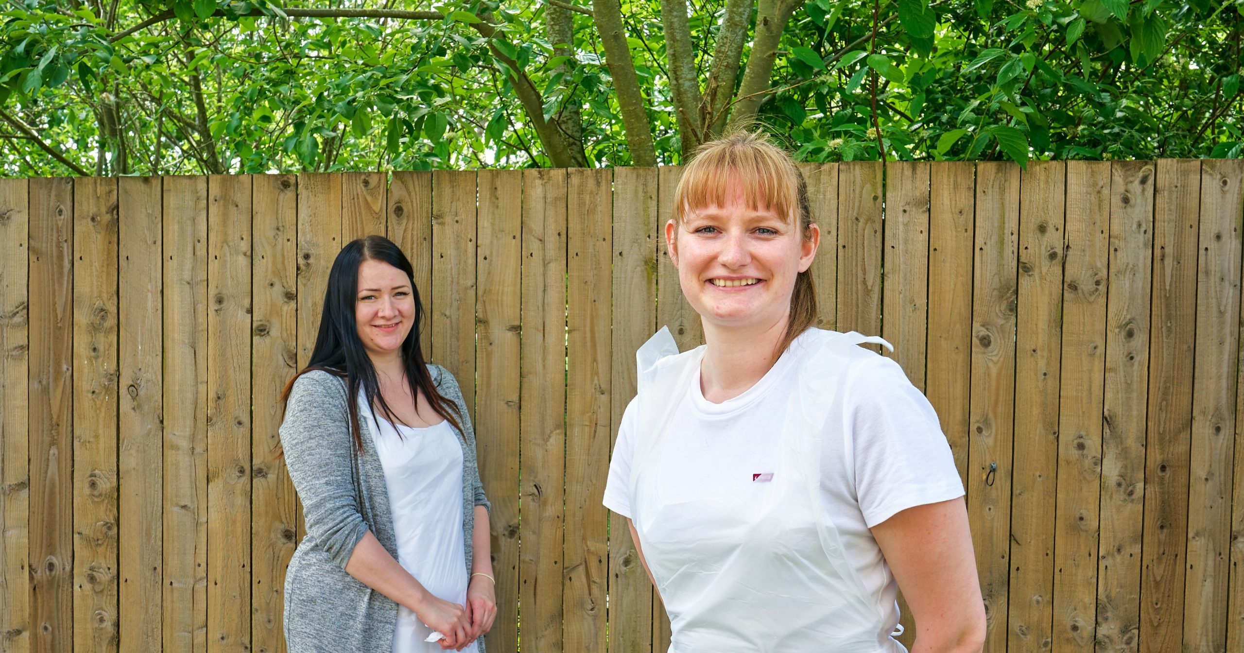 Two colleagues smiling against fence