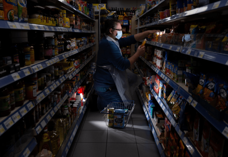 Francis. a support worker, kneeling down in a supermarket searching a shelf for produce.