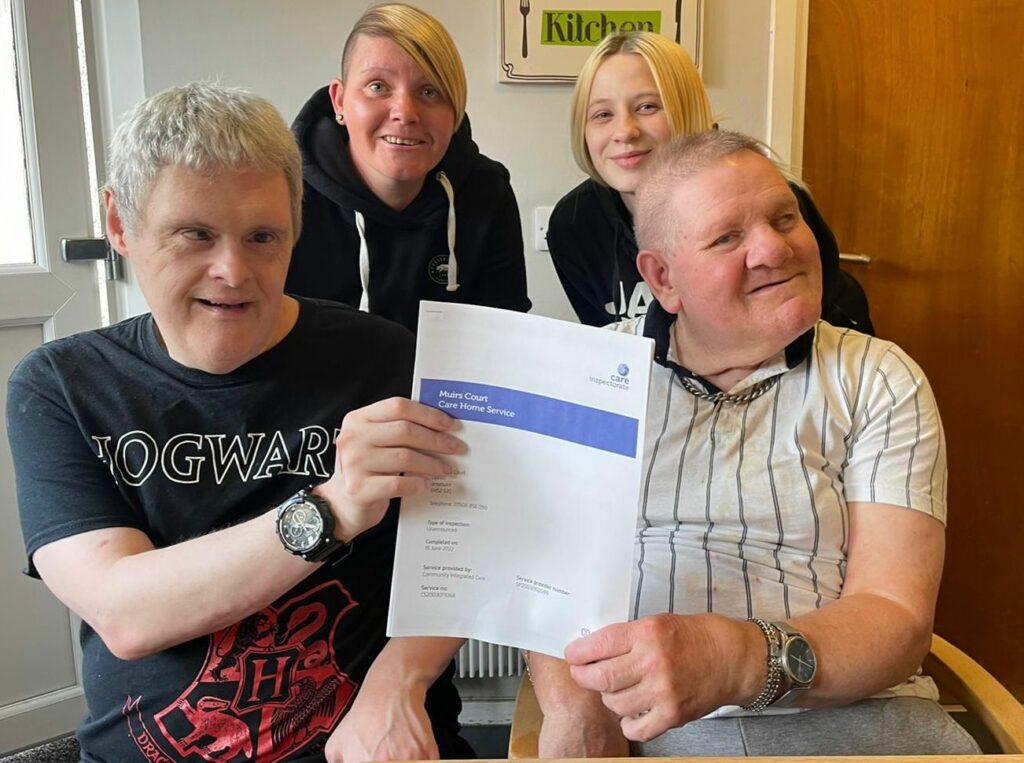 Colleagues and people supported by Muirs Court in Broxburn hold up their 'Very Good' Care Inspectorate report in celebration.