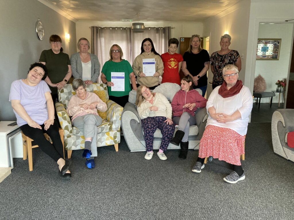 Colleagues and people supported at Mill Road and Lismore servcies in Armadale sit together, holding their 'Good' inspection reports.