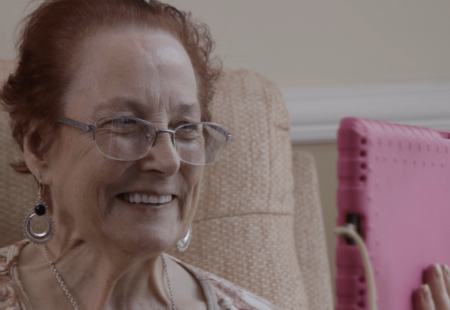 Woman with red hair and glasses, smiling and looking at a tablet.