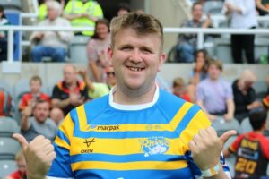 Declan, an LDSL player, smiling and giving a thumbs up to camera wearing a yellow and blue striped rugby shirt.