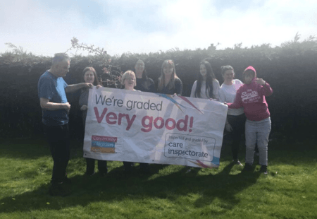 Colleagues and people supported at Colleonard Court in Banff hold a banner reading 'We're rated Very Good by the Care Inspectorate'