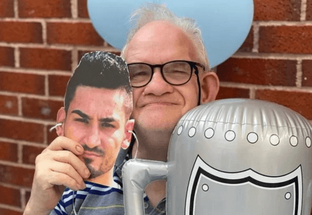 Person we support smiles, holding an Ilkay mask and inflatable Champions League trophy