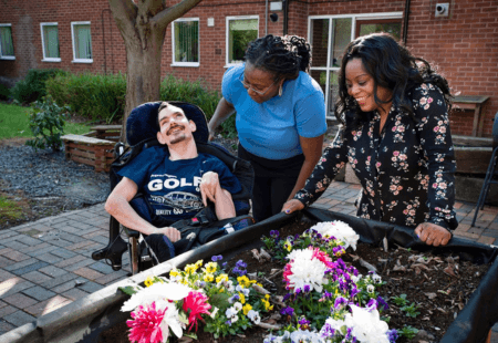 Sensory Gardening. Colleagues smiling with person we support in a wheelchair, at a garden planter.
