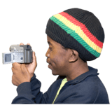Man wearing a hat with Jamacan coloured stripes, holding a video camera