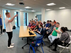 people sitting on chairs watching a man presenting at the front of the small room