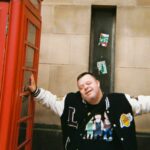 Media Inclusive Volunteer posing for a photograph between two red phone boxes.