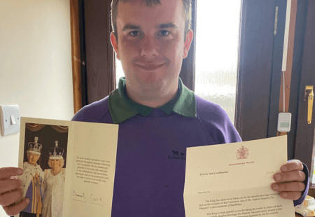 Kevin, a person supported by Community Integrated Care, holds a letter from the King's Royal Correspondent and a card signed by the King, with a picture of the King and Queen Consort.