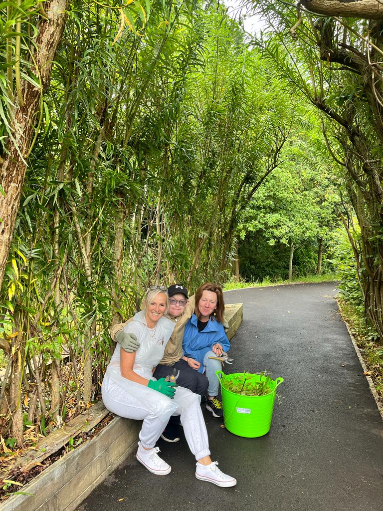 Three volunteers proudly sit amongst beautiful green tall grasses.