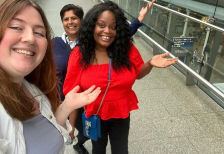 Aimee, Sushma and Gill stood pointing to the St Pancras station sign