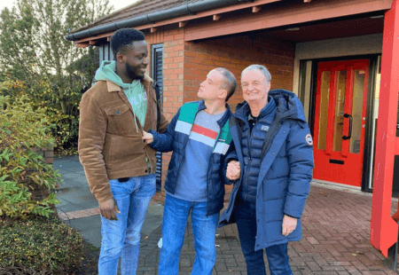 Support Worker (Omolulu), person supported (Philip) and Wallace Dobbin, Community Integrated Care Trustee) stand outside in front of Donald Dewar Court, smiling to camera. The visit took place as part of Trustee Week celebrations.