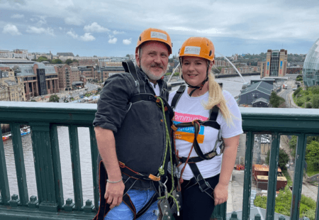 Colin and Codie stand in front of the Tyne Bridge in their helmets and harnesses, ready to Zipwire for charity.