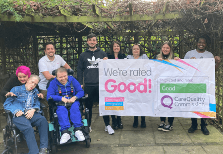 Colleagues and people supported at Tanners care home stand smiling celebrating their ratings with a banner reading 'We're rated Good by the CQC'
