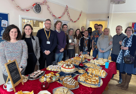 Colleagues and people we support in Leeds, at our Street Lane supported living service, gather around a buffet of festive treats with representatives from the department of health and social care and NCF.