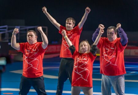 Inclusive volunteers in red t-shirts holding their arms up in unison as part of a dance routine.