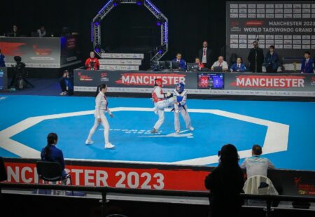 A taekwondo match taking place on a blue floor.