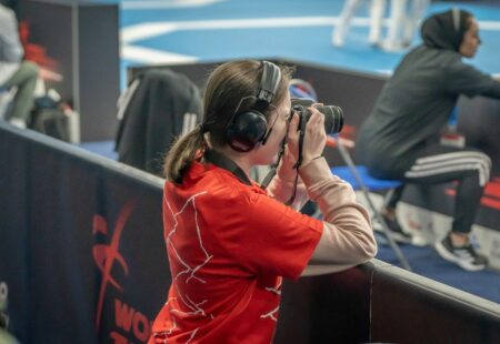 Inclusive volunteer in official red event t-shirt holding a large camera, taking a photograph of the event