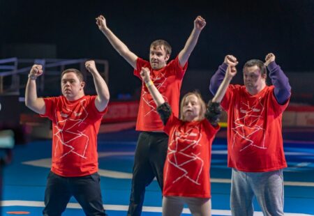 Inclusive volunteers in official event red t-shirts holding their hands up in celebration.