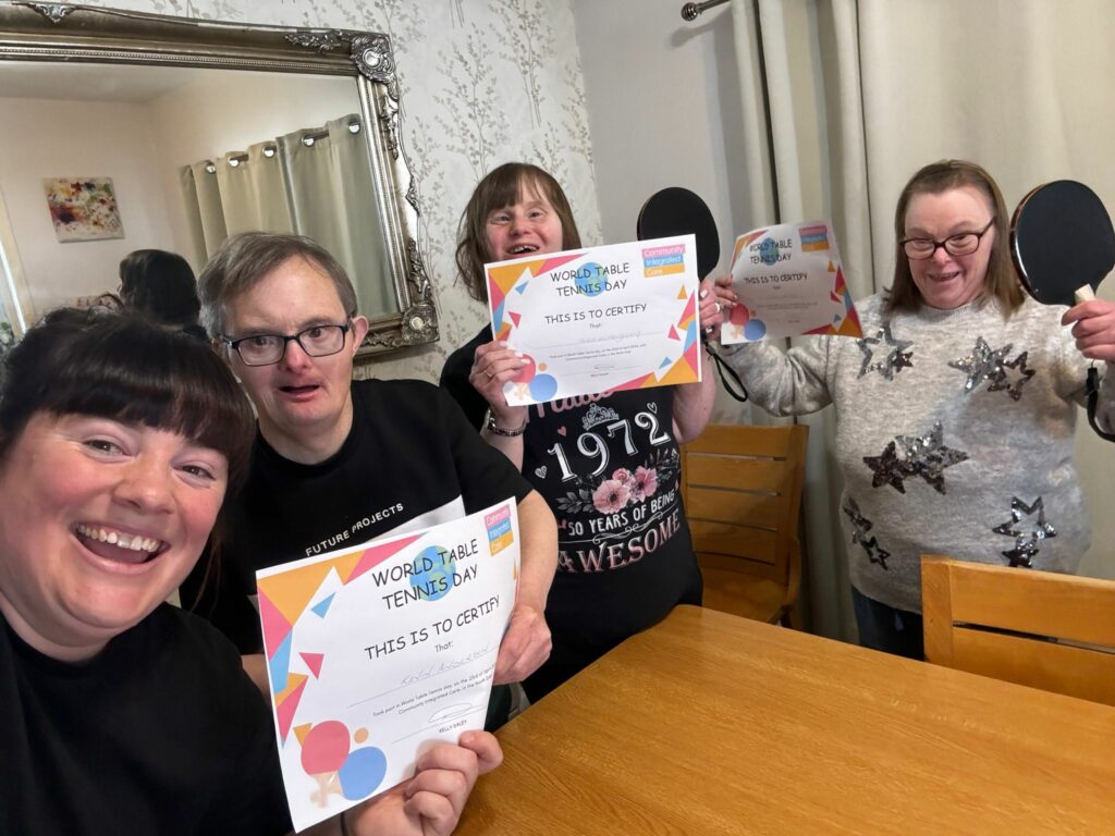 Colleagues and people supported by Community Integrated Care hold up participation certificates for World Table Tennis Day 2024.