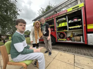 Two people we support standing with a guardian in front of a fire engine at Griffin Lodge Summer Fair 