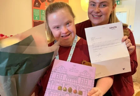 Amy is stood in her Costa Coffee uniform, with a guardian. She is holding flowers, a letter from Costa Coffee a box of chocolates. Both ladies are smiling at the camera