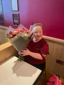Amy is sat down in Costa Coffee with a big bouquet of flowers. She is smiling happily with her gift