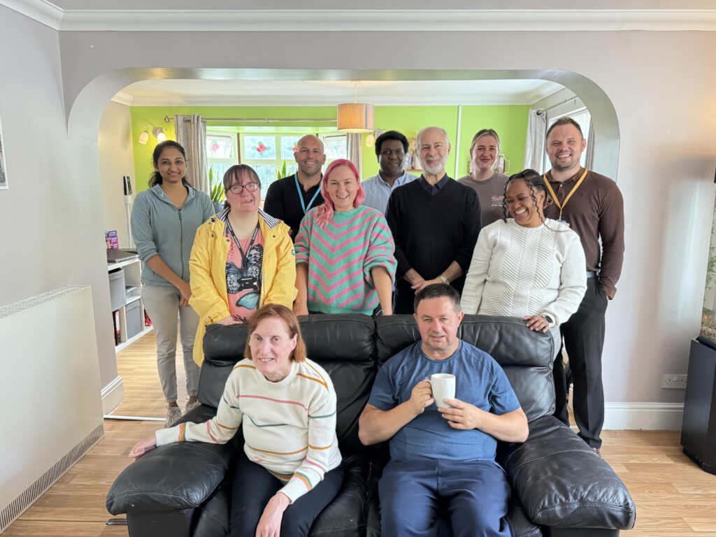 Fabian Hamilton MP, stands in a bright living room, surrounded by colleagues and people supported by Community Integrated Care. All are smiling to camera.