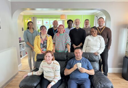 Fabian Hamilton MP, stands in a bright living room, surrounded by colleagues and people supported by Community Integrated Care. All are smiling to camera.