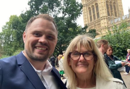 James Brind, Head of Operations, and Amandajayne Swann, Support Worker, smile to camera in a selfie-style photo. A parliamentary building can be seen behind them.