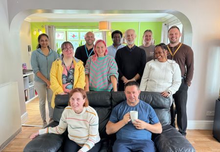 Fabian Hamilton MP, stands in a bright living room, surrounded by colleagues and people supported by Community Integrated Care. All are smiling to camera.