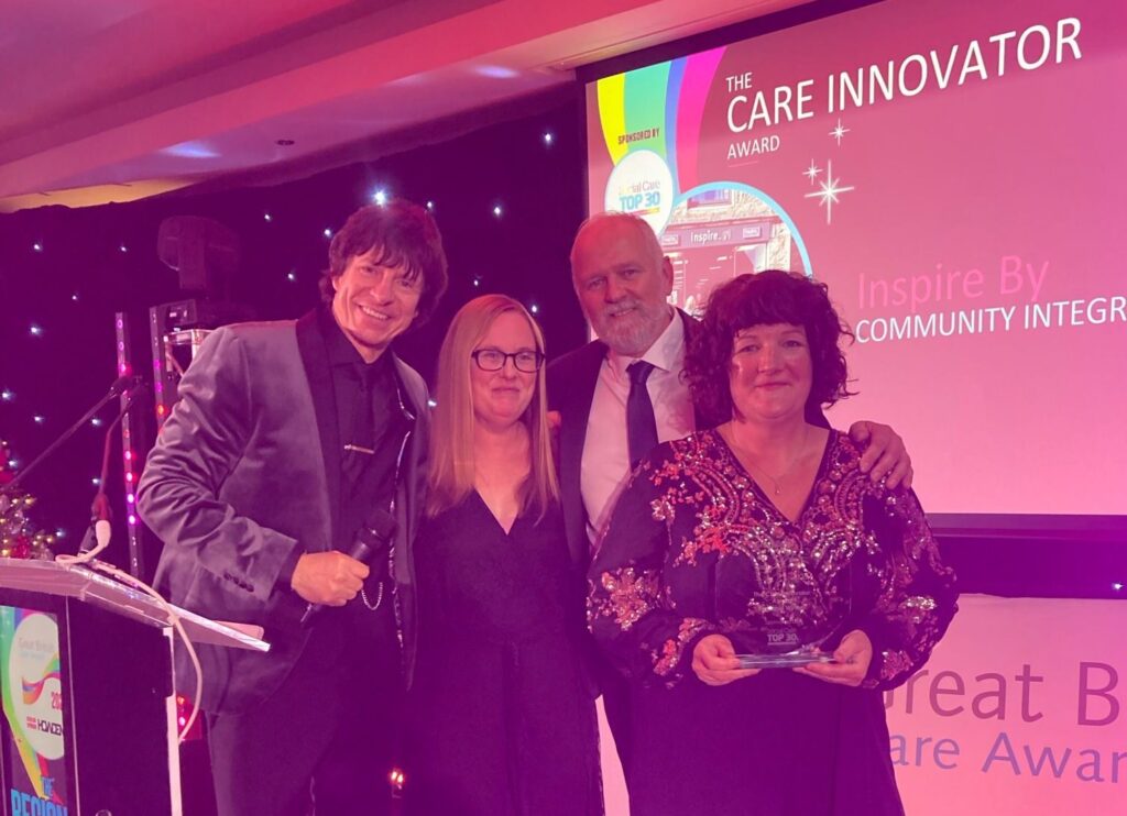 Three colleagues from the Inspire By team stand on stage collecting their trophy from the Great British Care Awards Scotland presenter.