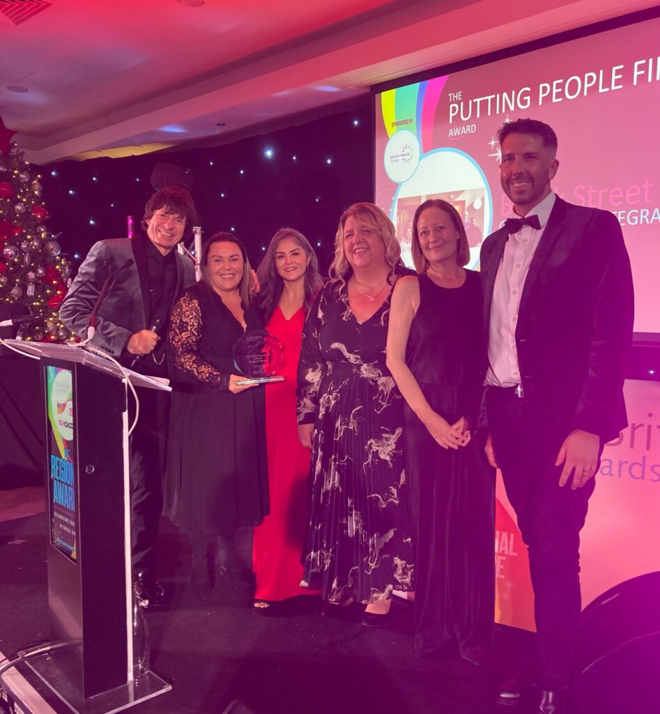 Four colleagues from the Brook Street team stand on stage collecting their trophy from the Great British Care Awards Scotland presenter.