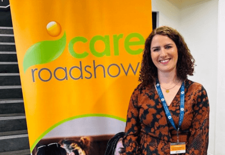 Sarah Mahoney, our Head of Employee Relations, stands in front of a Care Roadshows sign. She is smiling to camera.