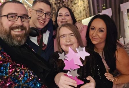 Colleagues from Community Integrated Care and people supported who starred in the Peter Pan Pantomime smile to camera for a selfie. They are holding their Celebrate Aberdeen Award with pride.