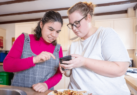 A colleague and a person we support stand in a kitchen, looking at a mobile device together.