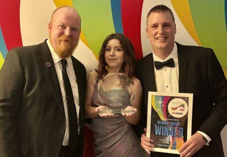 Three representatives from the Griffin Lodge eam stand holding their award. They are in black tie attire and smiling to camera.
