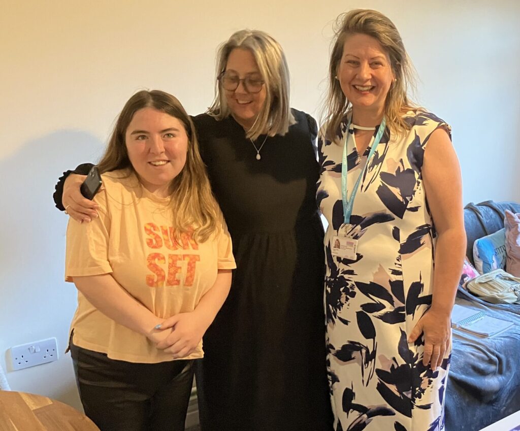 A person we support, colleague and Trustee (Imogen) stand together, smiling to camera.