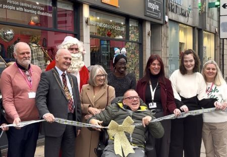 Colleagues and people supported by Community Integrated Care stand outside the Inspire By shop with the Lord provost of Aberdeen. They are all holding sparkly ribbon. Maurice (centre) is getting ready to cut the ribbon.