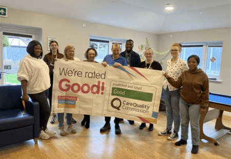 A group of colleagues smiling and holding a large banner which reads 'We're rated Good by the Care Quality Commission'