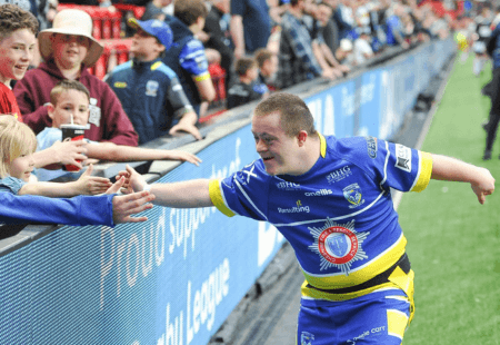 A Warrington Wolves Learning Disability Super League player is running off the pitch at Anfield, high fiving the crowd as he goes.