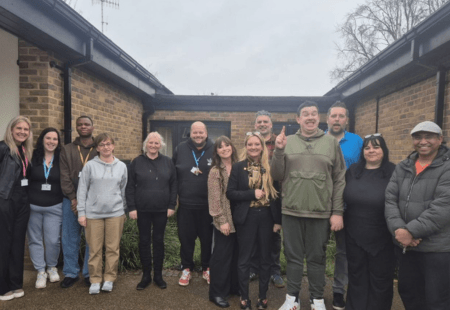 A group of colleagues and people we support stand outside in a Courtyard area with Amanda, smiling at the camera.