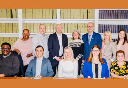 Gerard stands in front of a table with 11 other sector leaders, all smiling to camera. They are wearing professional attire and are stood in front of rows of folders.