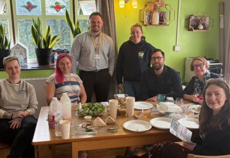 Seven people sat around a dining table, smiling to camera.