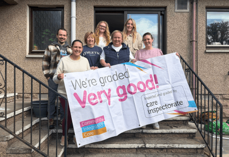 Colleagues are smiling and holding up a banner reading 'We're rated Very Good by the Care Inspectorate'.